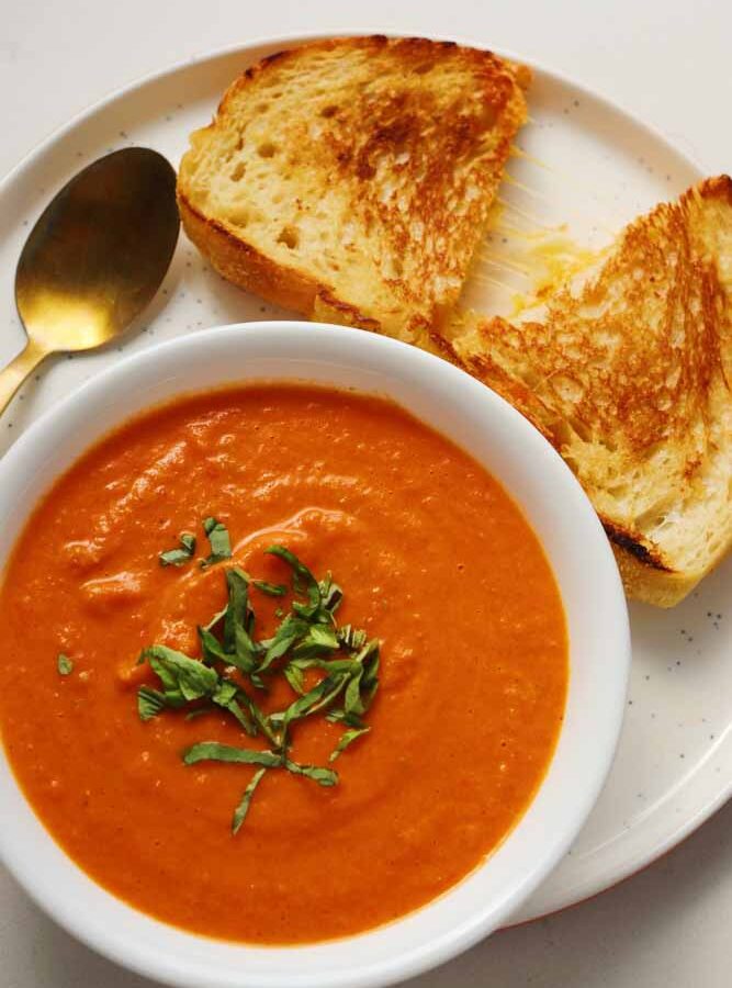 grilled cheese and tomato soup on a white plate with a white bowl and a golden spoon.