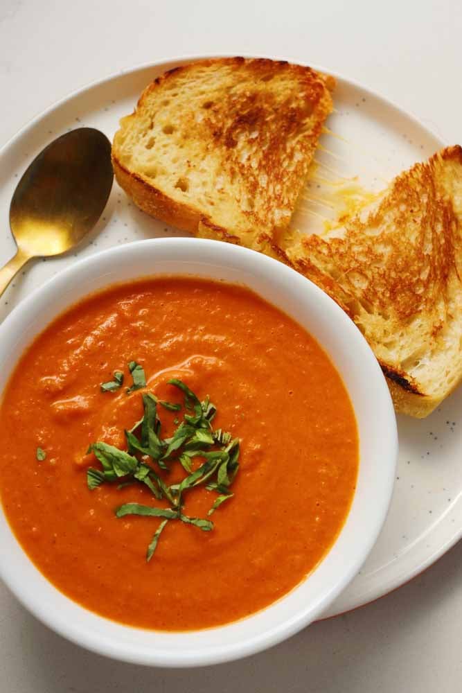 grilled cheese and tomato soup on a white plate with a white bowl and a golden spoon. 