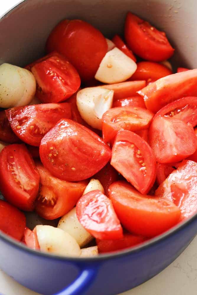 fresh cut tomatoes and onions in a large dutch oven about to get roasted and turned into soup. 