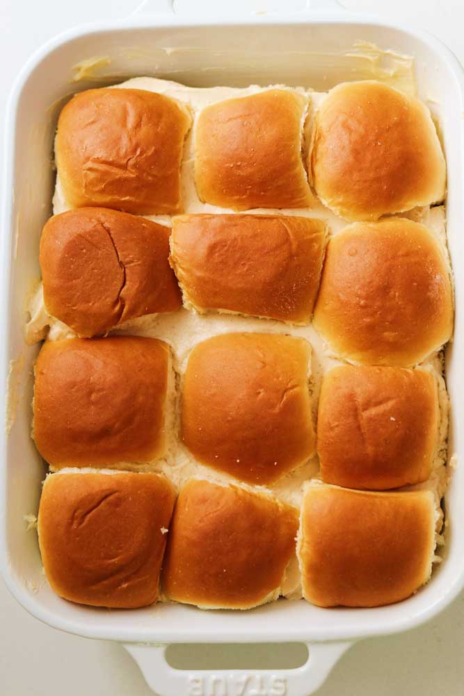 Kings Hawaiian rolls in a white casserole dish filled with brown sugar cream cheese filling. 