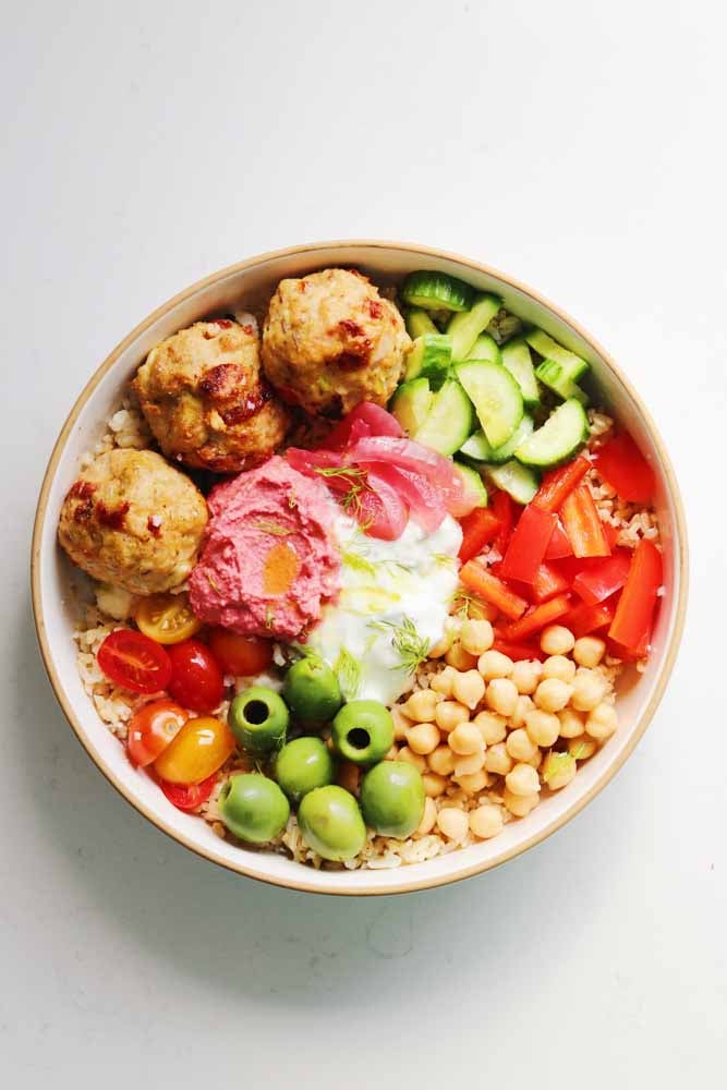 a white mediterranean rice bowl filled with colorful ingredients.