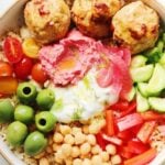 a colorful mediterranean rice bowl with chicken, tzatziki, fresh veggies and hummus.
