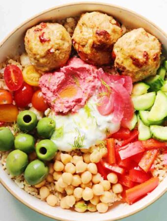 a colorful mediterranean rice bowl with chicken, tzatziki, fresh veggies and hummus.