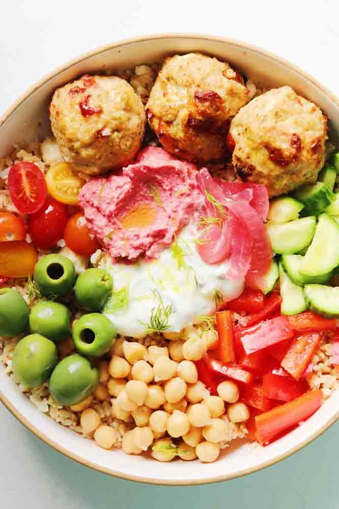 a colorful mediterranean rice bowl with chicken, tzatziki, fresh veggies and hummus. 