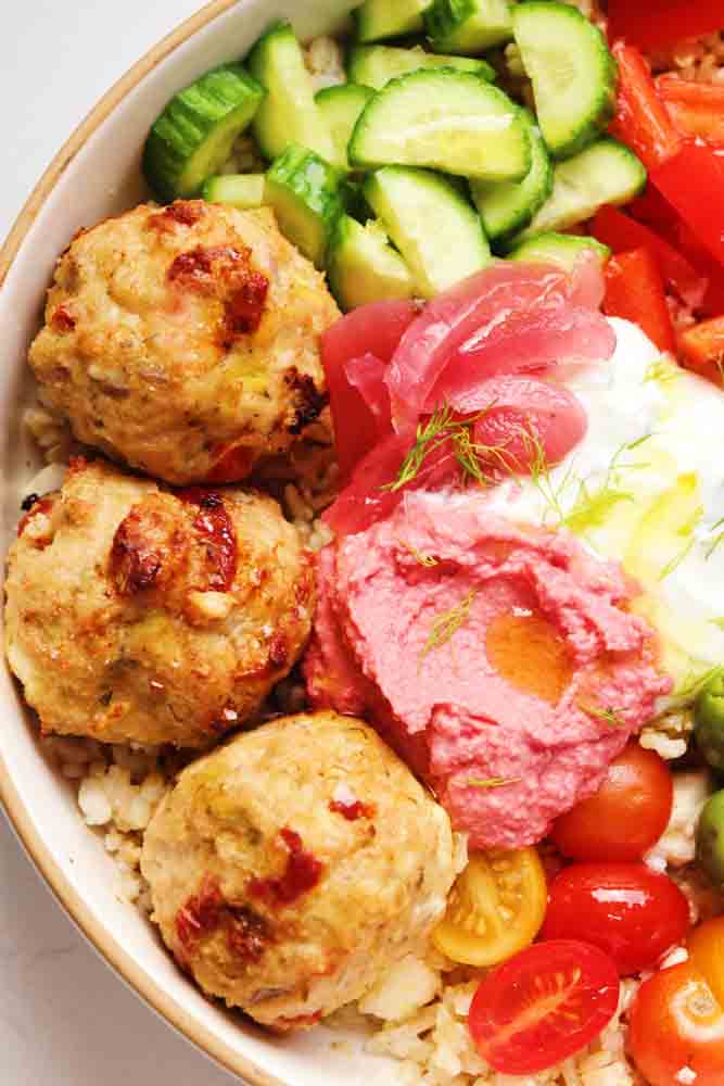 an up close view of mediterranean chicken meatballs on top of a rice bowl. 