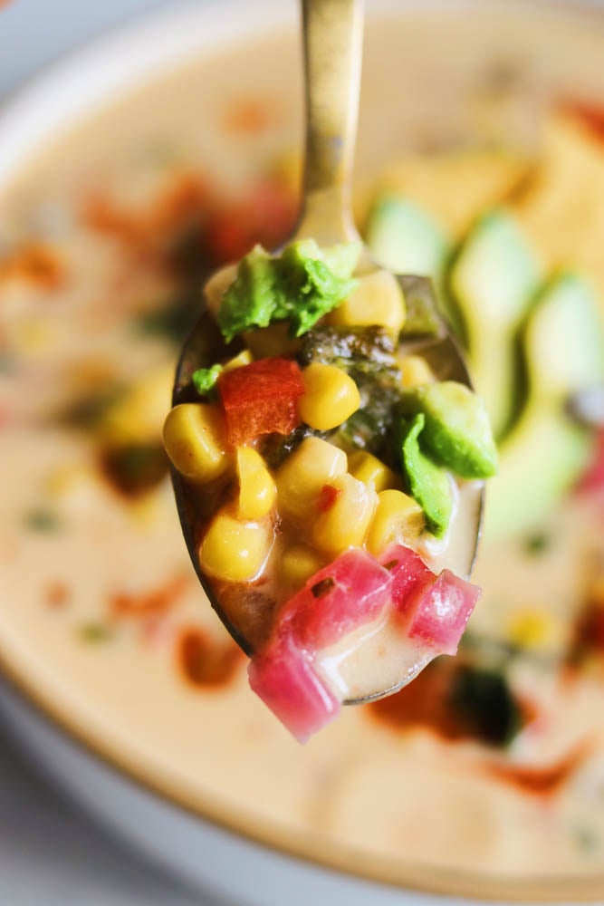 a golden spoon holding the colorful ingredients of mexican street corn soup. 