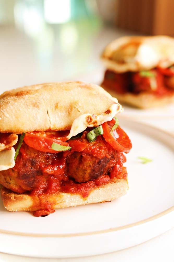 a pepperoni pizza meatball sub sandwich on a white plate with one behind it. 