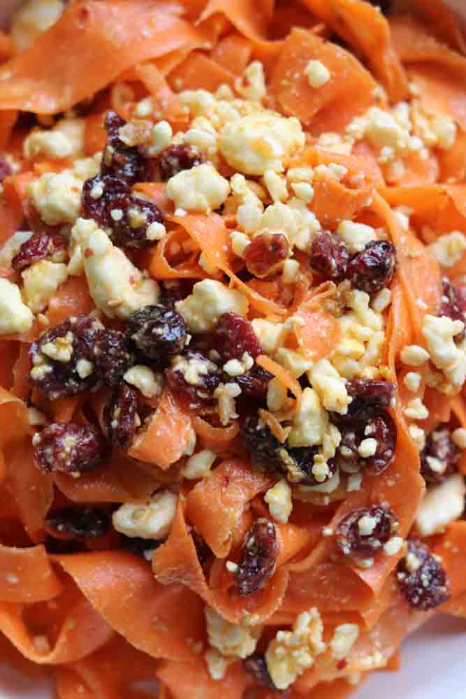 an up close view of the birght orange carort ribbons, feta, and dried cranberries in a bowl. 