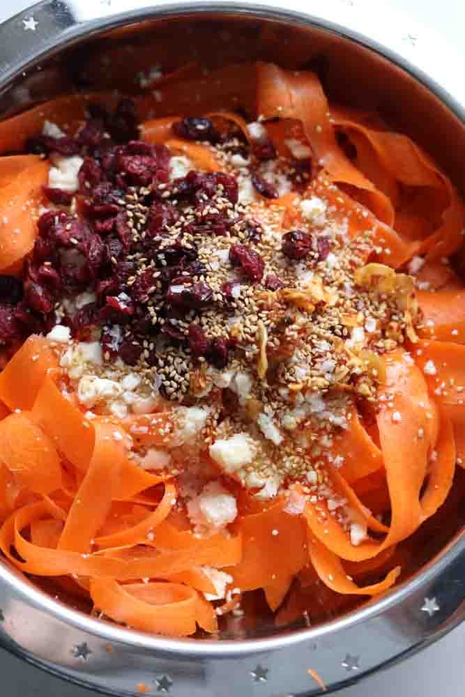 carrot ribbons topped with sesame seeds, feta, and dried cranberries in a silver bowl.
