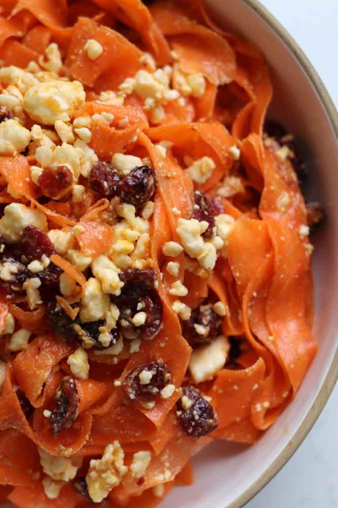 the right side of a white bowl filled with bright orange carrot salad.