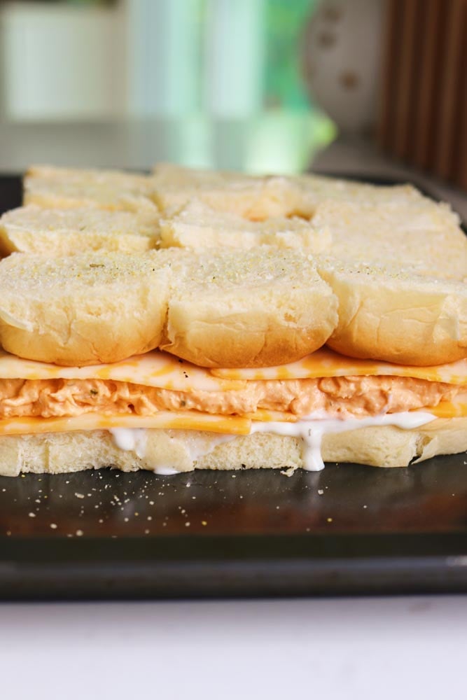 a baking sheet topped with uncooked buffalo chicken sliders. 