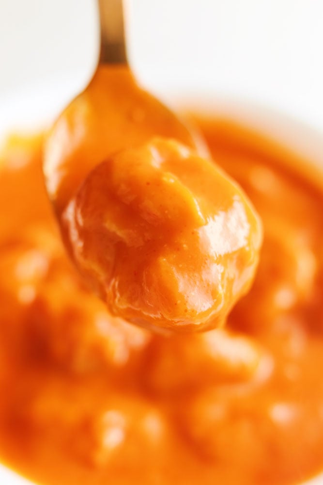 a cheese dumpling covered in tomato soup sitting on a golden spoon. 