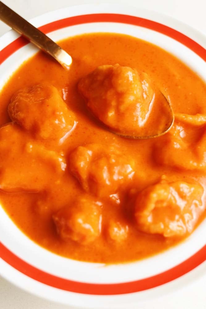 a golden spoon sitting in a bowl of cheese dumpling tomato soup. 