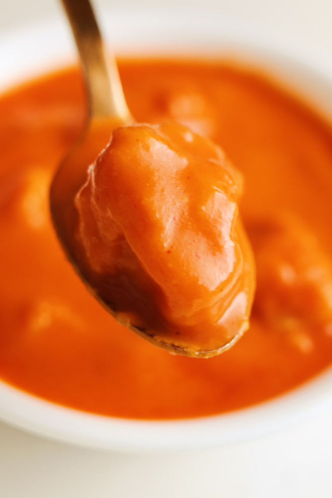 a gold spoon holding up a cheese dumpling over a bowl of tomato soup. 