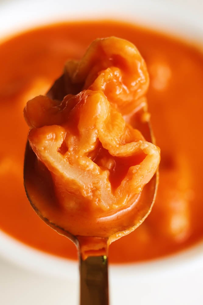 a halved cheese dumpling being held over a bowl of tomato soup.