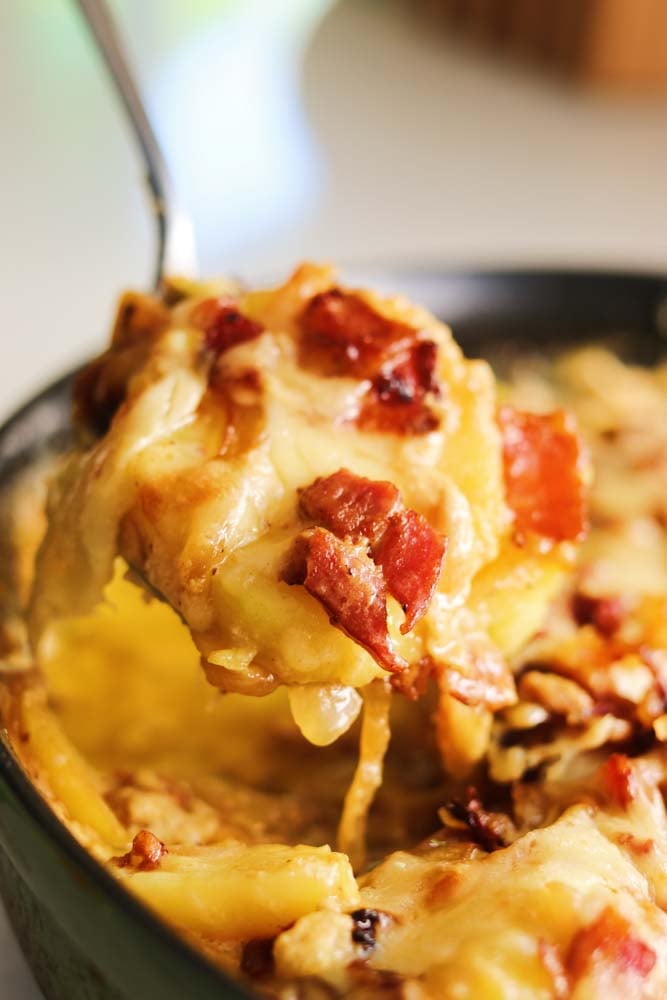 a heaping spoonful of tartiflette comte over a cast iron skillet.