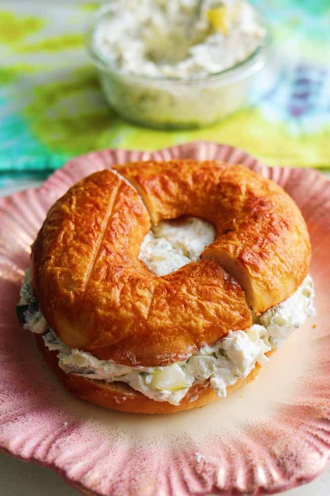a toasted cheese bagel filled with dill pickle cream cheese on a pink plate. 