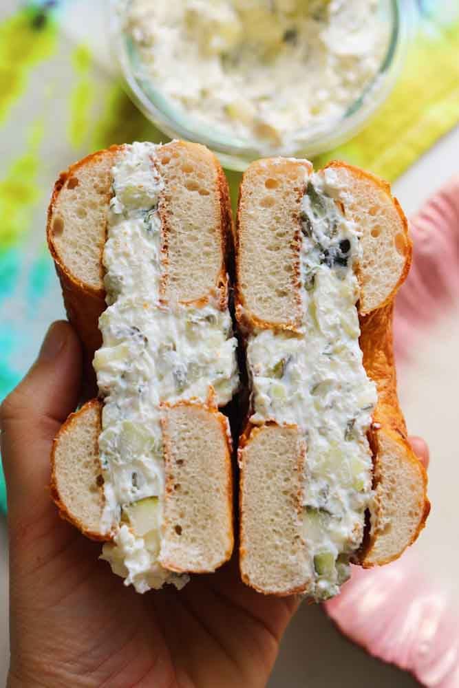 a hand holding a bagel schmeared with dill pickle cream cheese.