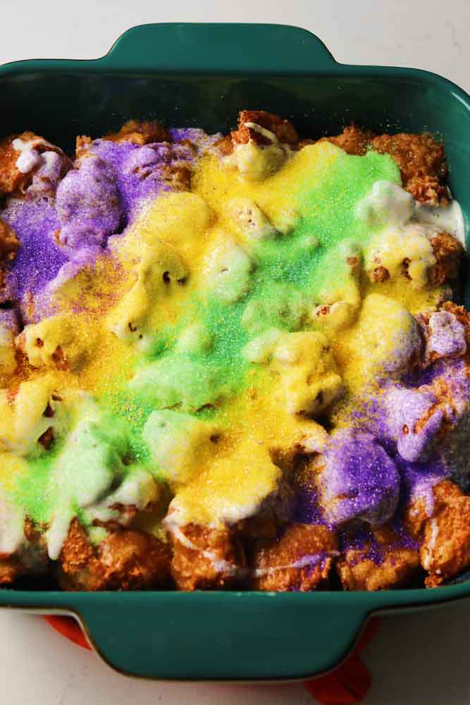 yellow, purple and green sprinkles covering a teal baking dish full of king cake monkey bread.