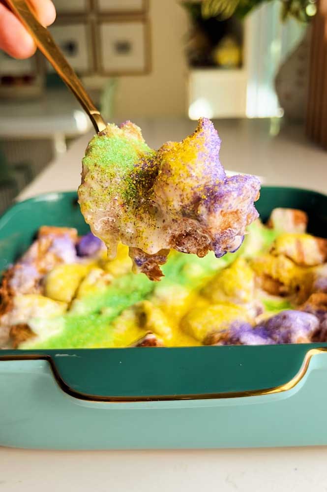 a teal baking dish full of king cake monkey bread with a spoon holding a serving over the top of it. 