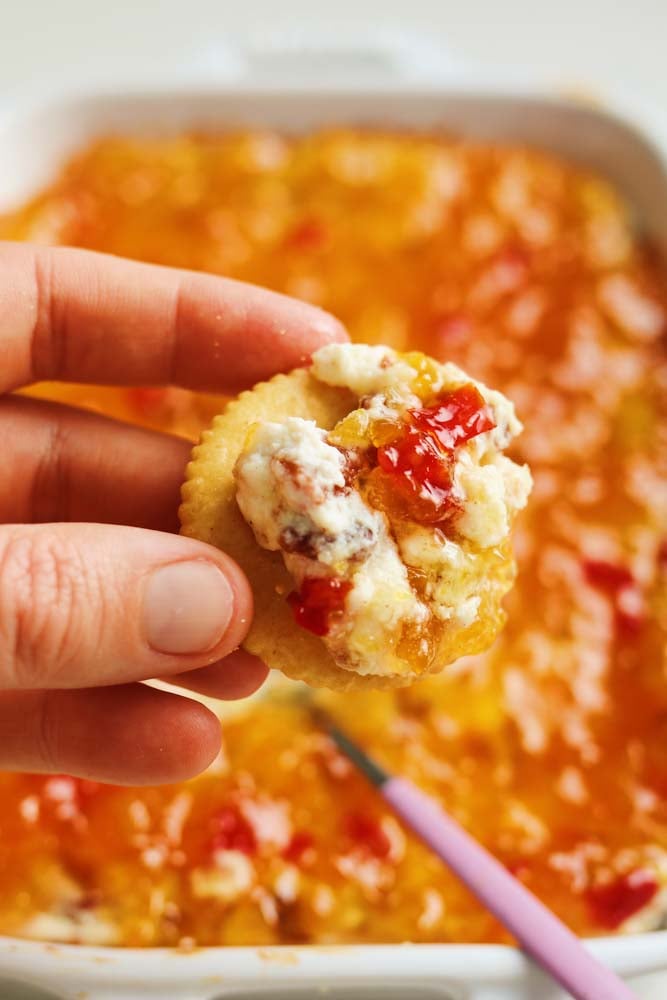 a hand holding a ritz cracker smothered in pepper jelly cheese dip. 
