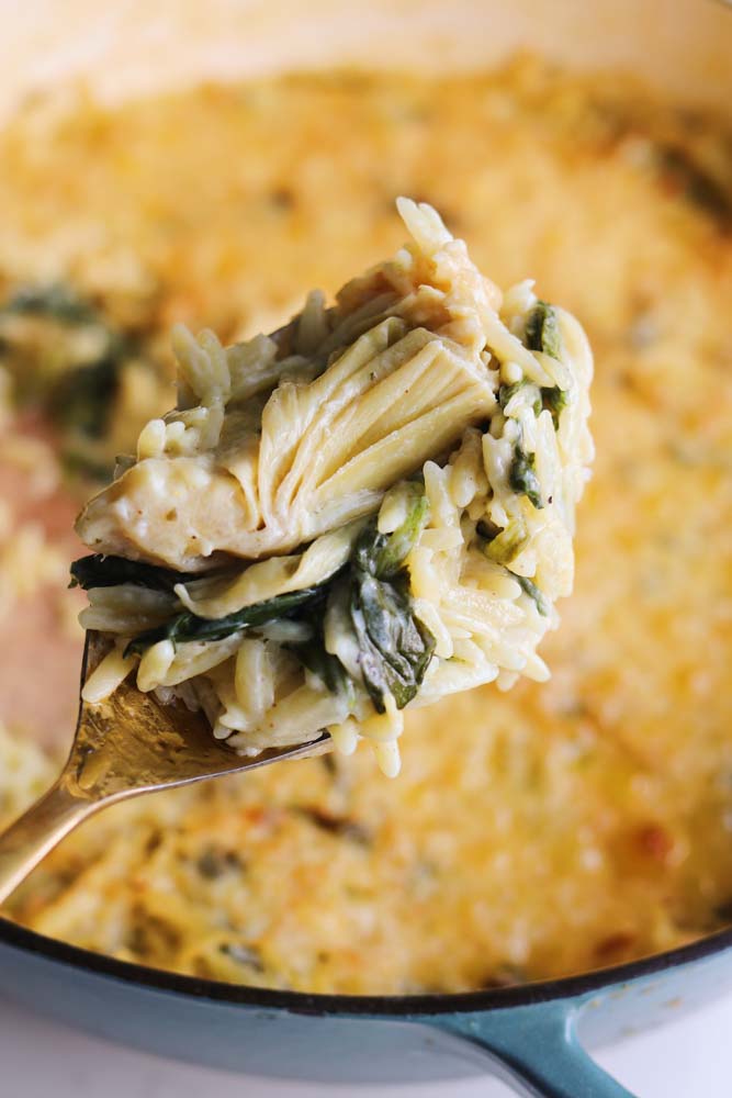 a gold spoon holding a scoop of spinach artichoke orzo.