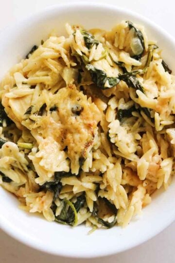 spinach artichoke orzo in a white bowl.