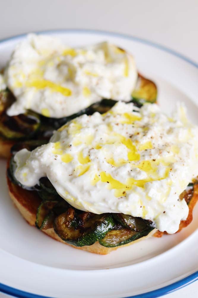 two pieces of zucchini burrata toast on a white plate with a blue outline. 