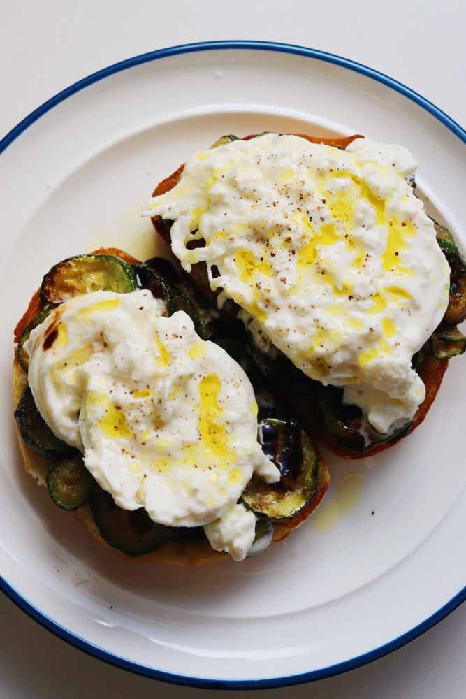 a white plate topped with two pieces of zucchini burrata toast. 