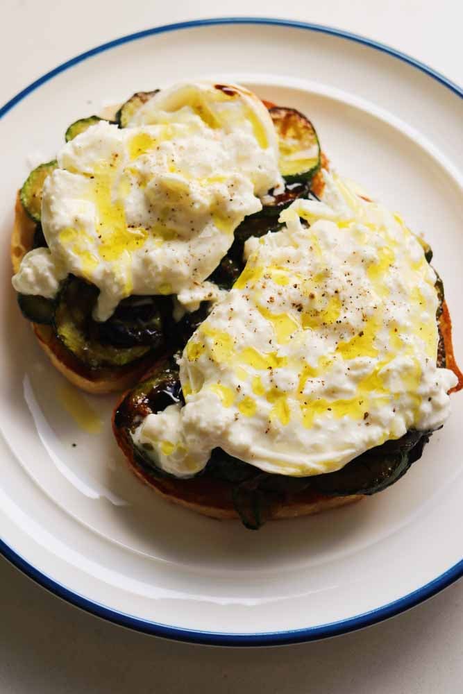 a white plate topped with zucchini burrata toast. 