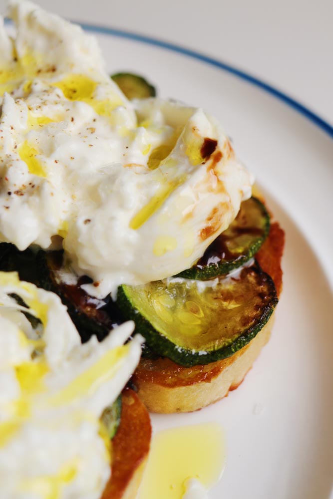 an up close view of a piece of zucchini burrata toast. 