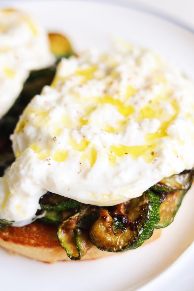 two pieces of zucchini burrata toast on a white plate. 