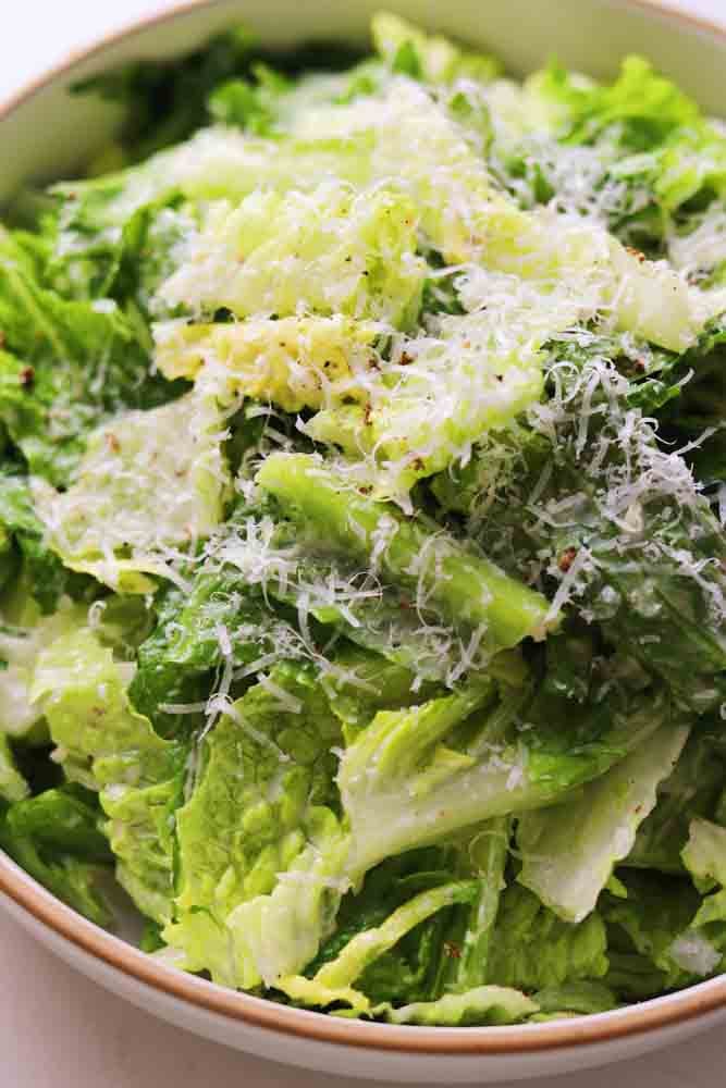 an up close view of a white bowl of caesar salad without anchovies