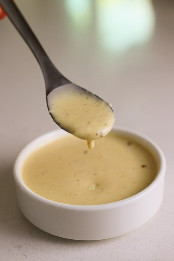 miso caesar salad dressing in a white bowl with a spoon dipped into it. 
