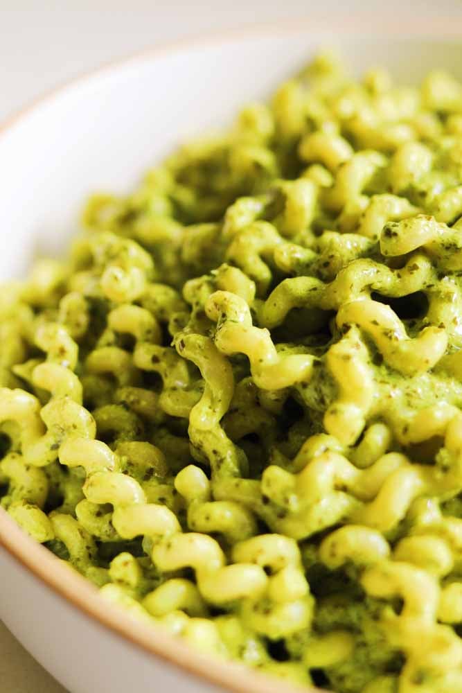 a macro view of twirly pasta noodles coated in a vibrant green pasta sauce. 