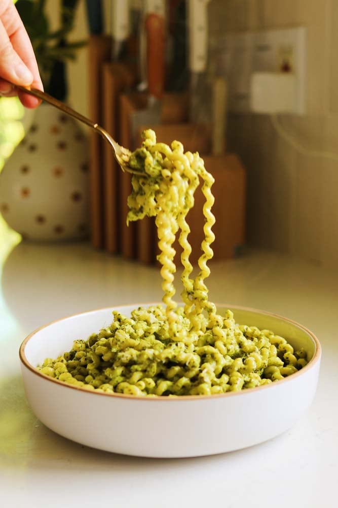 a bowl of pasta with green pasta sauce with a fork swirling some of the noodles.