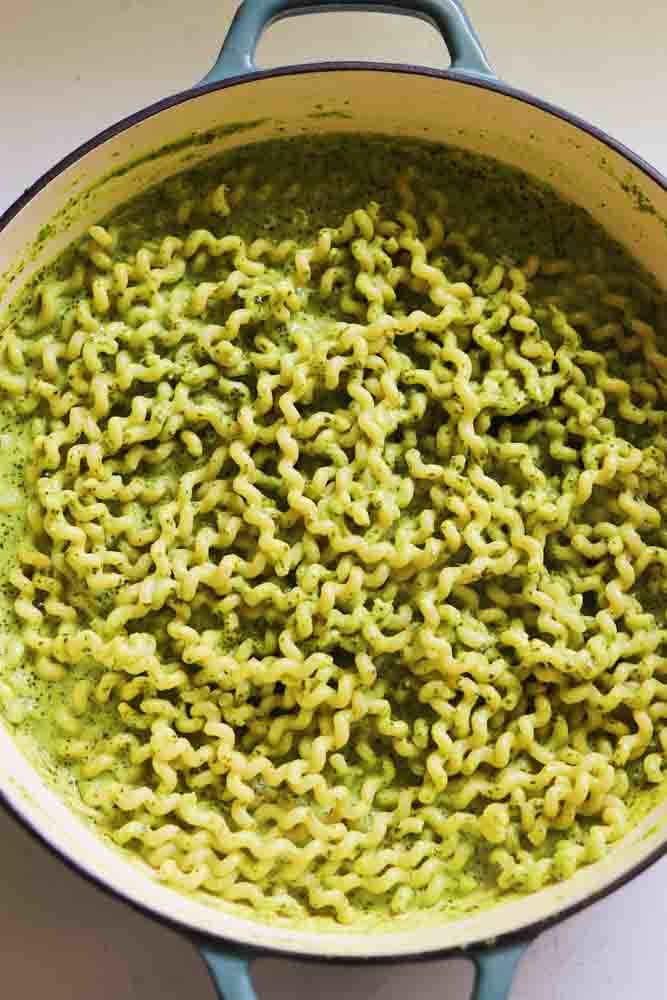 a blue braising pot filled with pasta coated in green pasta sauce. 