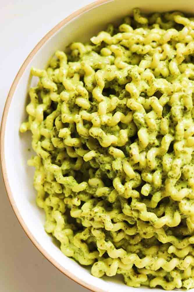 the left side of a white bowl of pasta with green pasta sauce. 