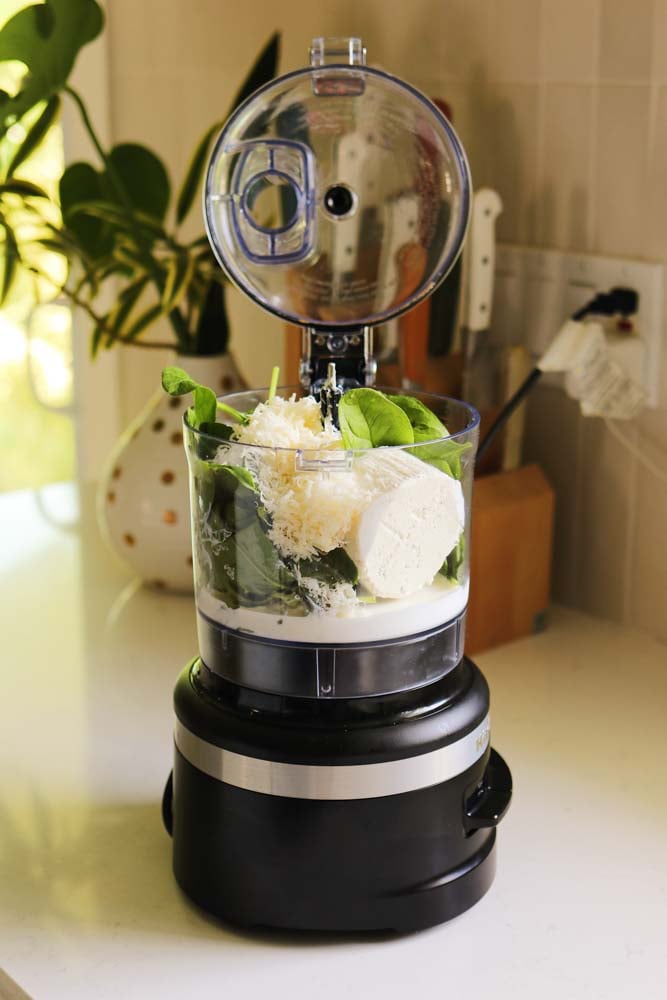 a food processor filled with spinach, cheese, cream, and a few other ingredients. 