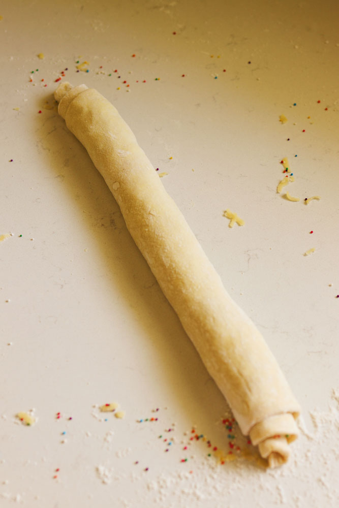 a puff pastry log rolled up on white countertop.
