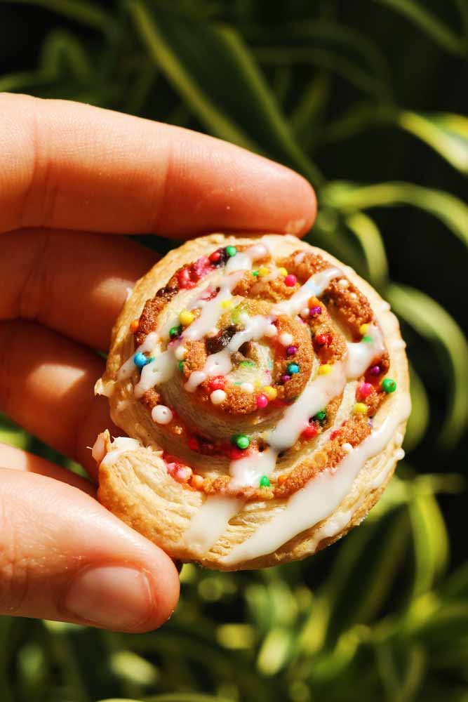 a hand holding a single rainbow almond croissant swirl.