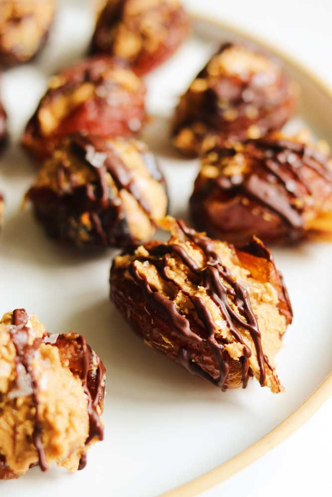 the right side of a white plate topped with chocolate drizzled stuffed medjool dates. 