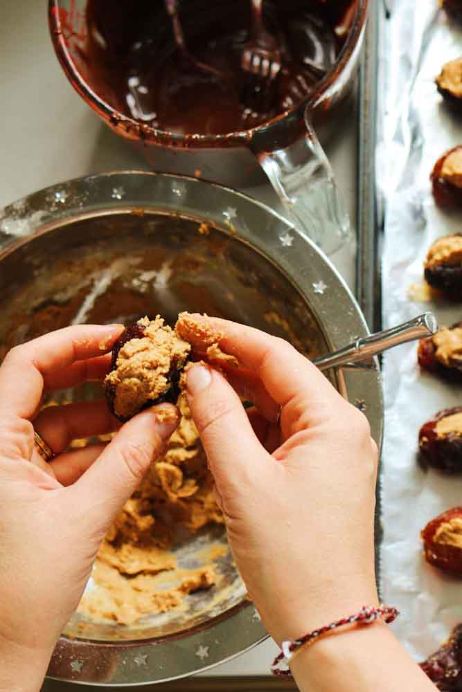 two hands stuffing medjool dates with peanut butter and protein powder. 
