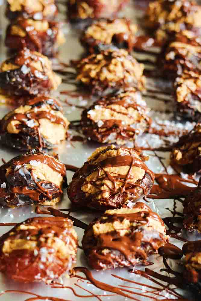 a baking sheet full of stuffed dates with peanut butter being drizzled with chocolate. 