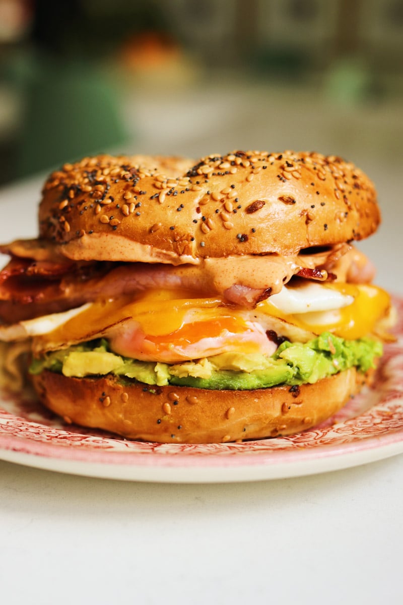 a colorful bagel sandwich sitting on a pink plate. 