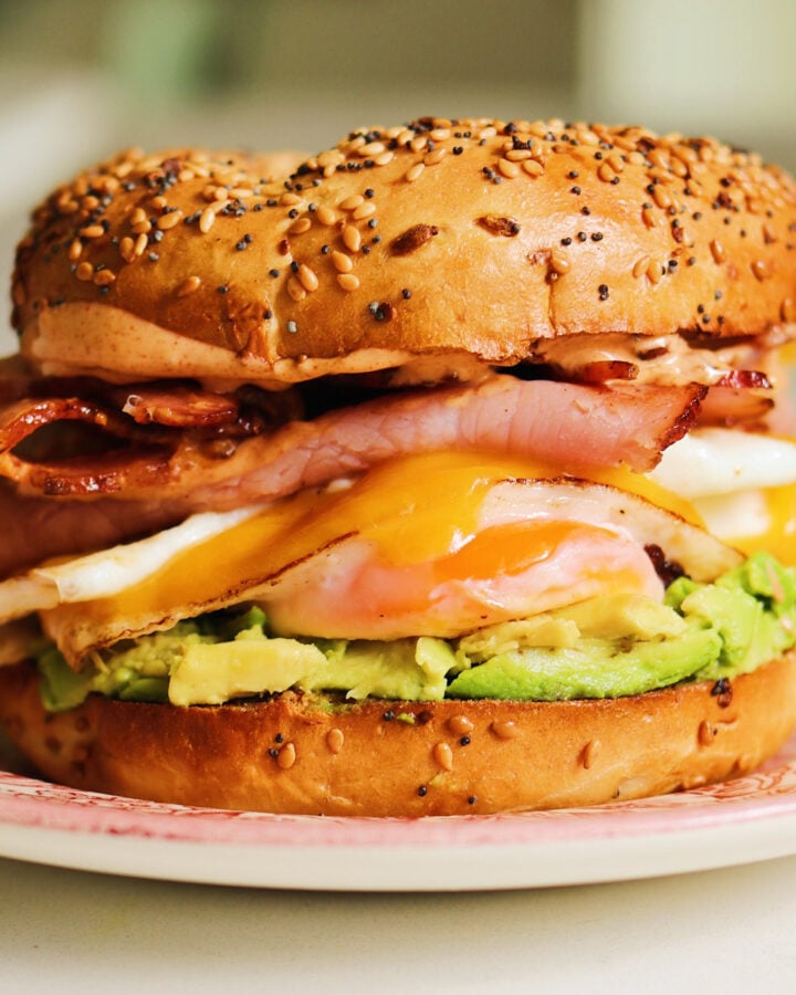 a bagel breakfast sandwich with colorful layers sitting on a pink plate.