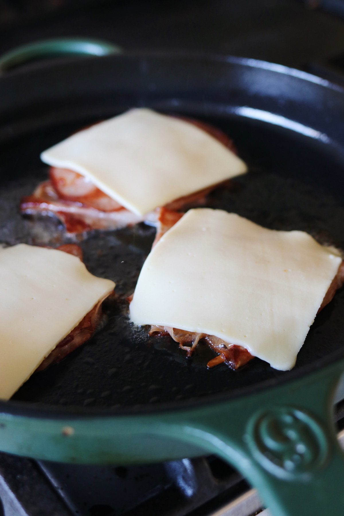 white slices of cheese over piles of crispy mortadella in a fry pan. 
