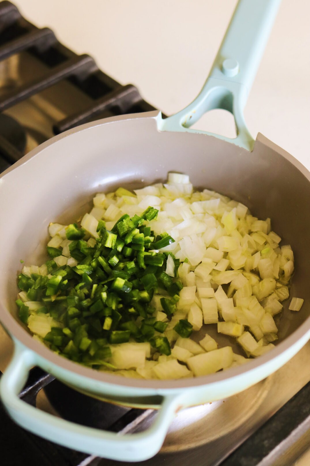 a blue fry pan cooking chopped jalapenos and onions on a stovetop. 