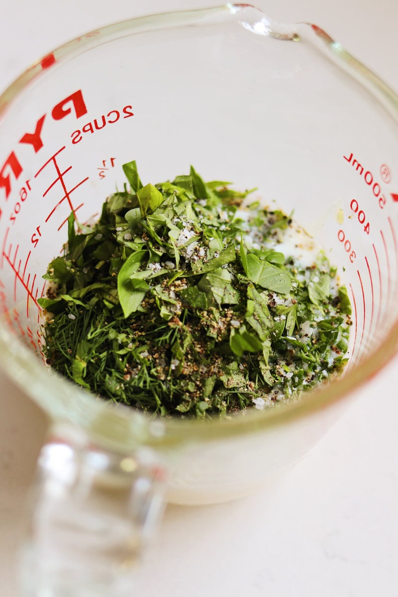 a pyrex measuring cup filled with creamy dressing made of butttermilk and herbs.