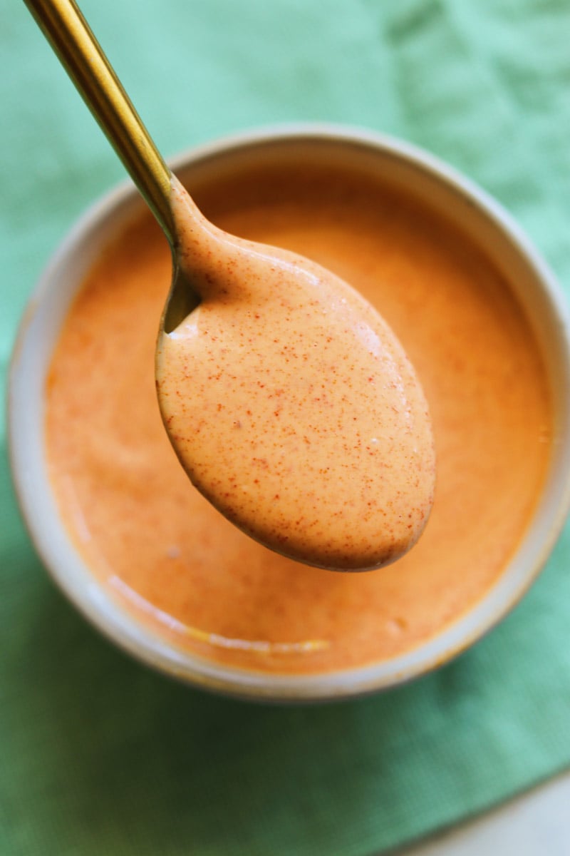 a golden spoon dunking into a bowl of creamy sriracha sauce.